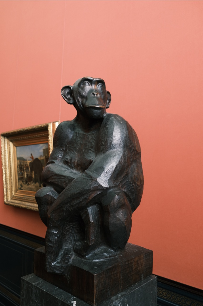 一个猴子的雕塑。石猴蹲坐并且双手搭在膝盖上，头扭向右边望去。猿猴天生在鼻子和嘴巴中间拉长的脸形使其表情有一种“我不在乎”的神韵
