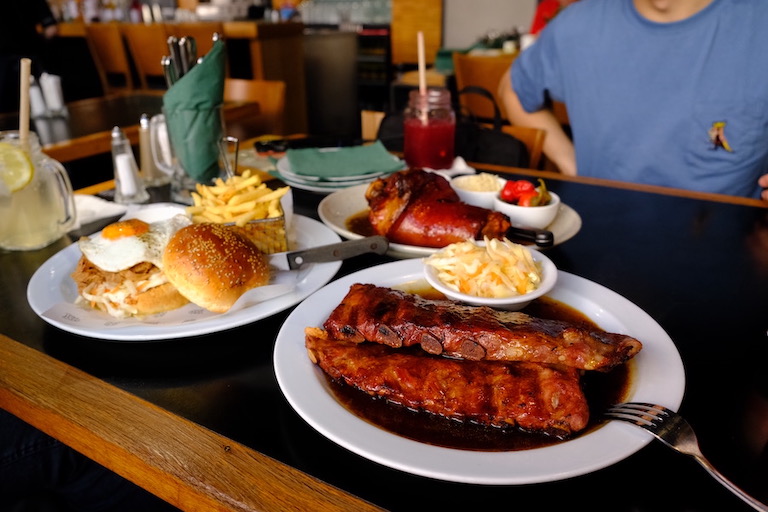 一张桌子上面有三道菜，烧猪肋排，烧猪蹄，和手撕猪肉汉堡配薯条